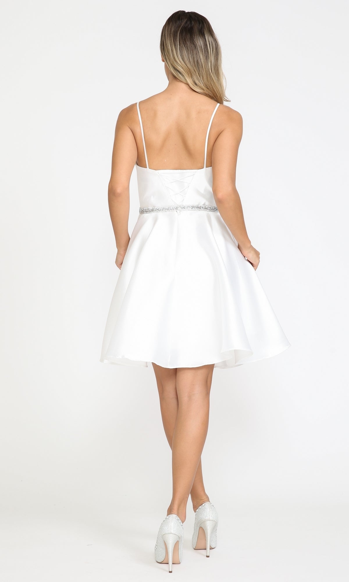 A woman in the Short Mikado Homecoming Dress 8420 with pockets and thin straps, paired with silver heels, stands facing away against a white background. This stylish party dress is available for under $150.